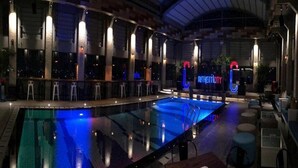 An indoor swimming pool with a glass barrier, bar stools, and a neon sign reading "Authenticity". - The Excelton Hotel (Palembang)