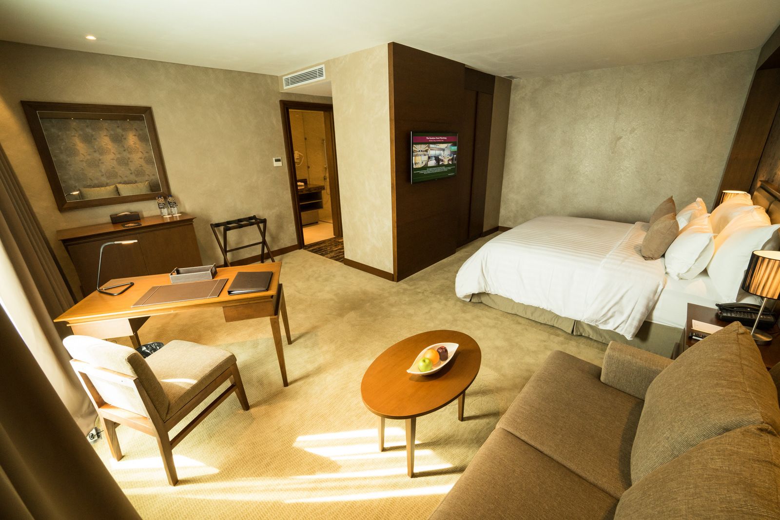 A hotel room with a bed, a desk, a chair, a sofa, and a small table with fruit.