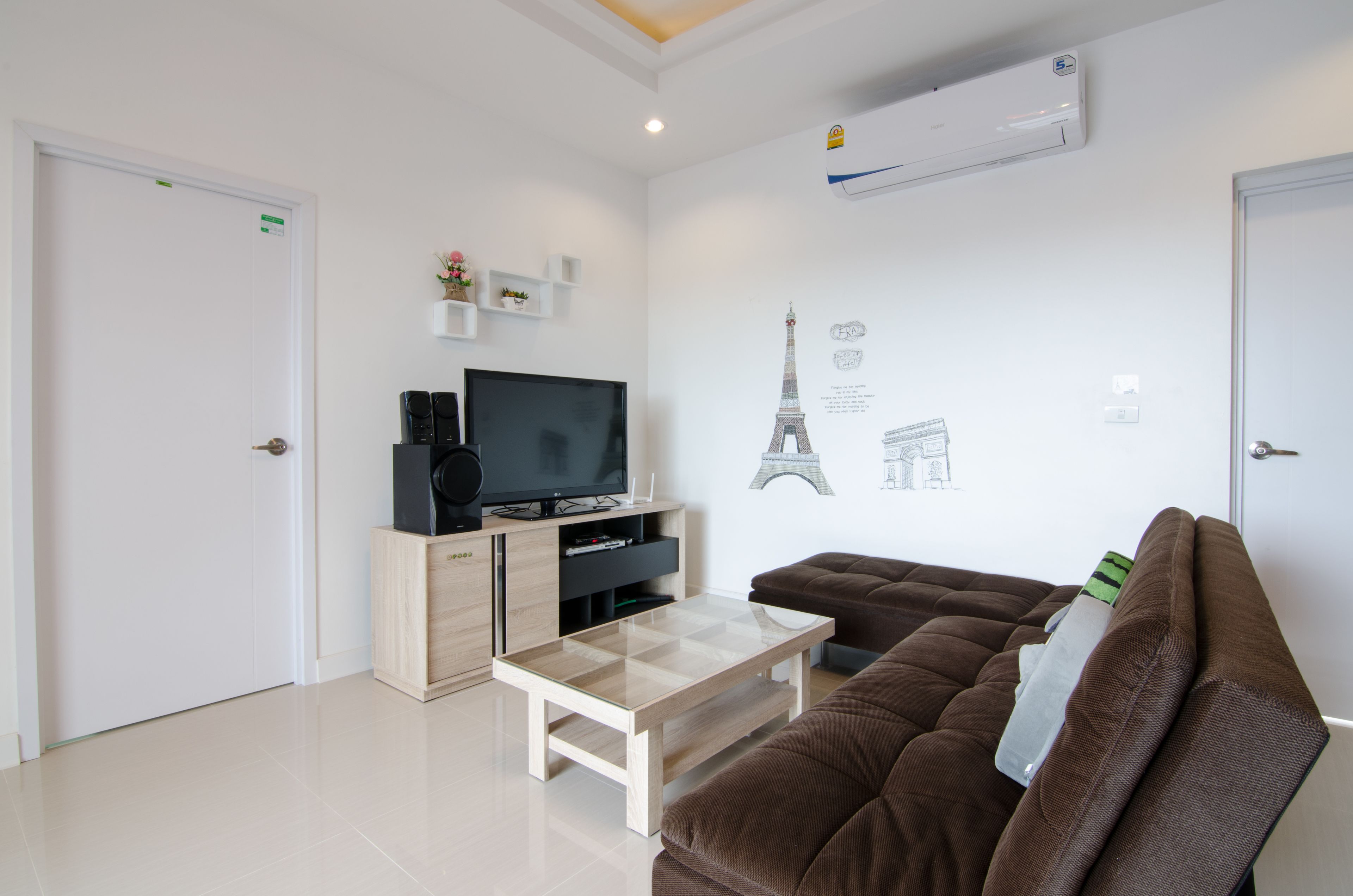 A modern living room with a flat-screen TV, a wooden coffee table, a brown sofa, and a wall-mounted air conditioner.