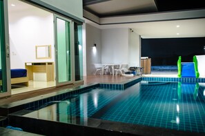 A modern indoor swimming pool with clear blue tiles, a wooden deck, and a seating area with chairs and a table. - Le Leaf Pool Villa 6 (Hua Hin)