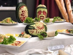 Ein Tisch mit verschiedenen Speisen, darunter eine kunstvoll geschnitzte Wassermelone und ein Teller mit Schriftzug 