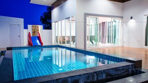 A modern indoor swimming pool with clear blue tiles, a wooden deck, and glass doors leading to a bright room. - Le Leaf Pool Villa 7 (Hua Hin)