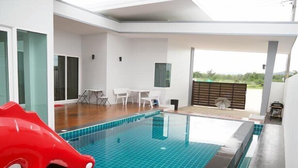 A modern indoor swimming pool with a clear blue tiled floor, surrounded by white walls and a wooden deck area. - Le Leaf Pool Villa 7 (Hua Hin)