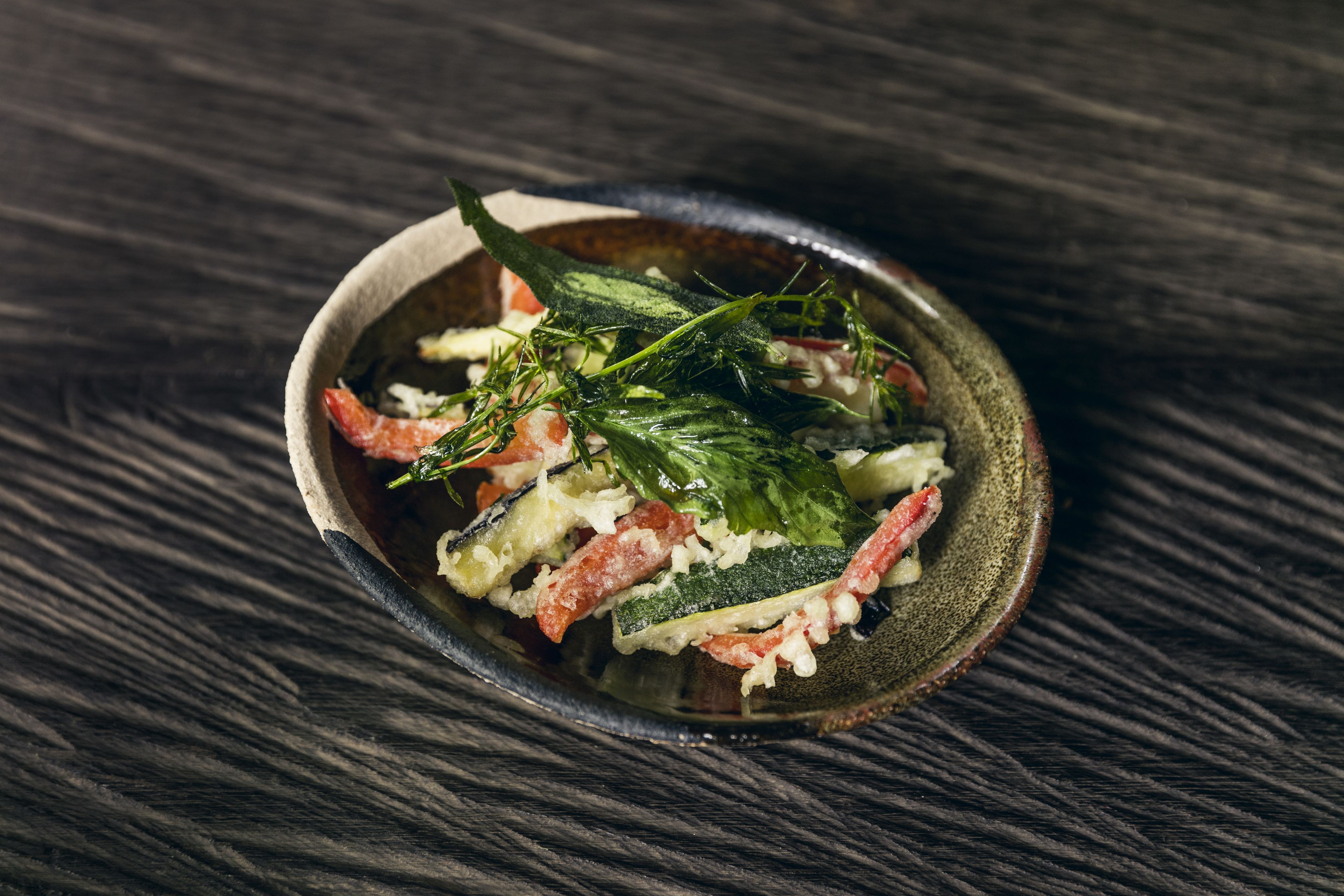 Uma salada com vários vegetais e ervas sobre uma superfície de madeira escura.