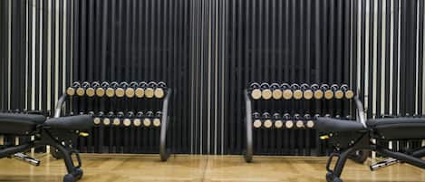 A room with two black office chairs and a row of dumbbells against a wall with vertical blinds.