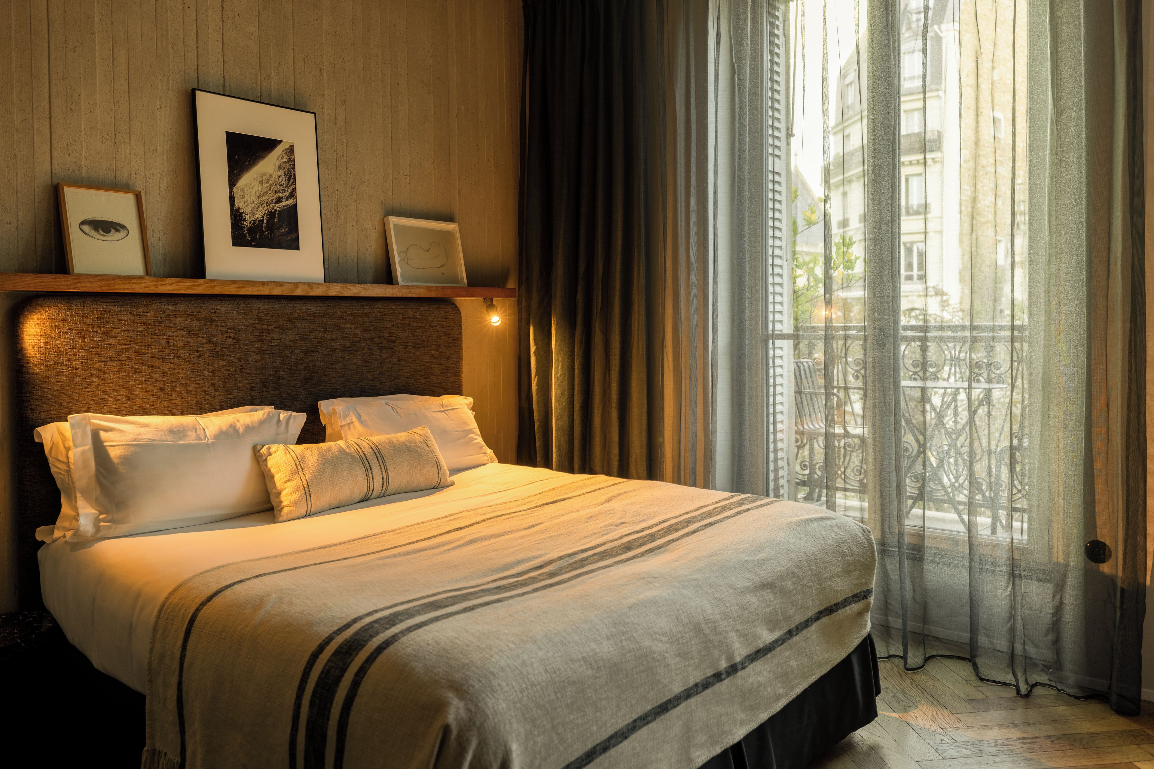 Habitación de hotel con cama, cabecera, ventana con cortinas y vista a edificios.