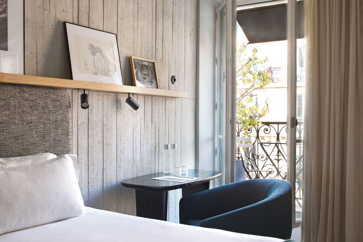 Habitación de hotel con cama, una mesita, una silla y un balcón con vistas.