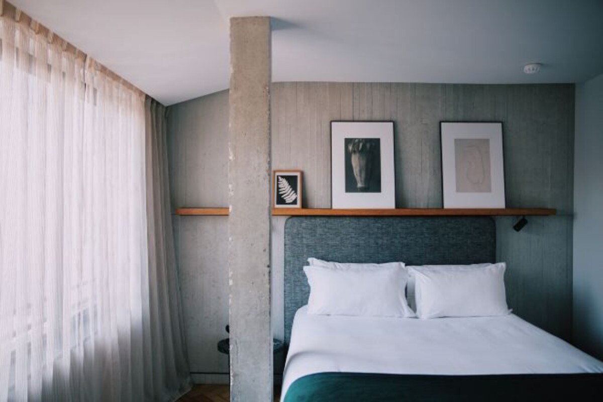 Ett modernt hotellrum med en stor säng, en sänggavel och två inramade tavlor på väggen.