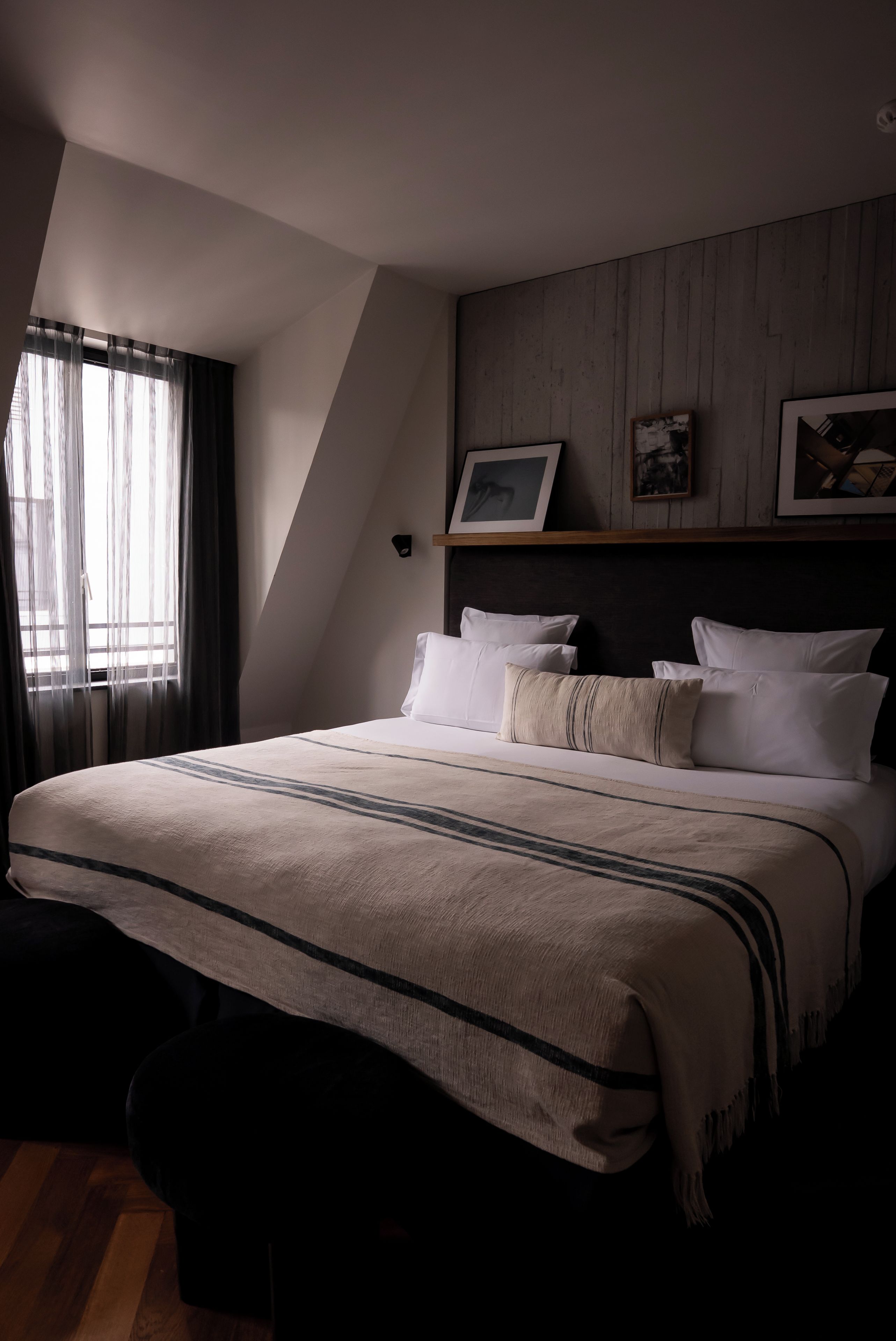 A bedroom with a bed, a window with curtains, a wooden headboard, and two framed pictures.