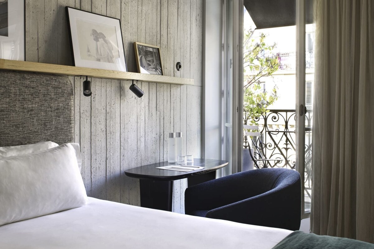 Een hotelkamer met een bed, een tafeltje, een stoel en een balkon met uitzicht.