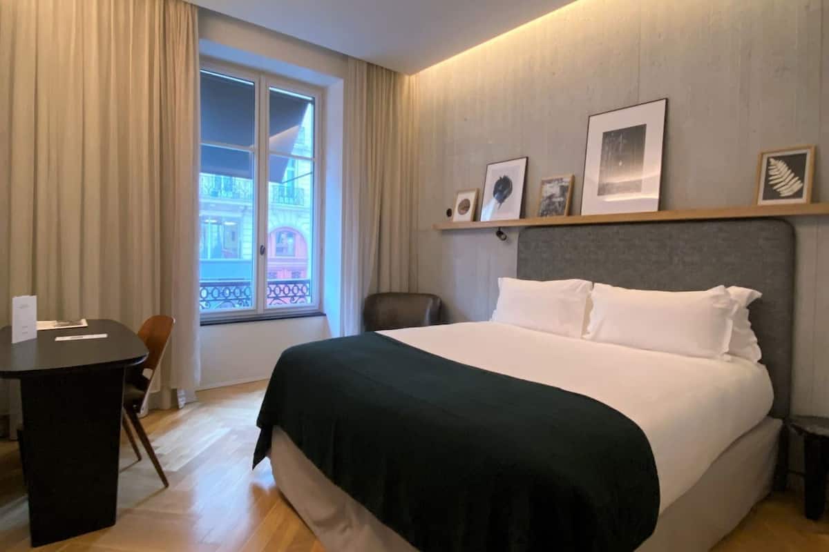 Habitación de hotel con una cama grande, un escritorio y vistas a un edificio desde la ventana.
