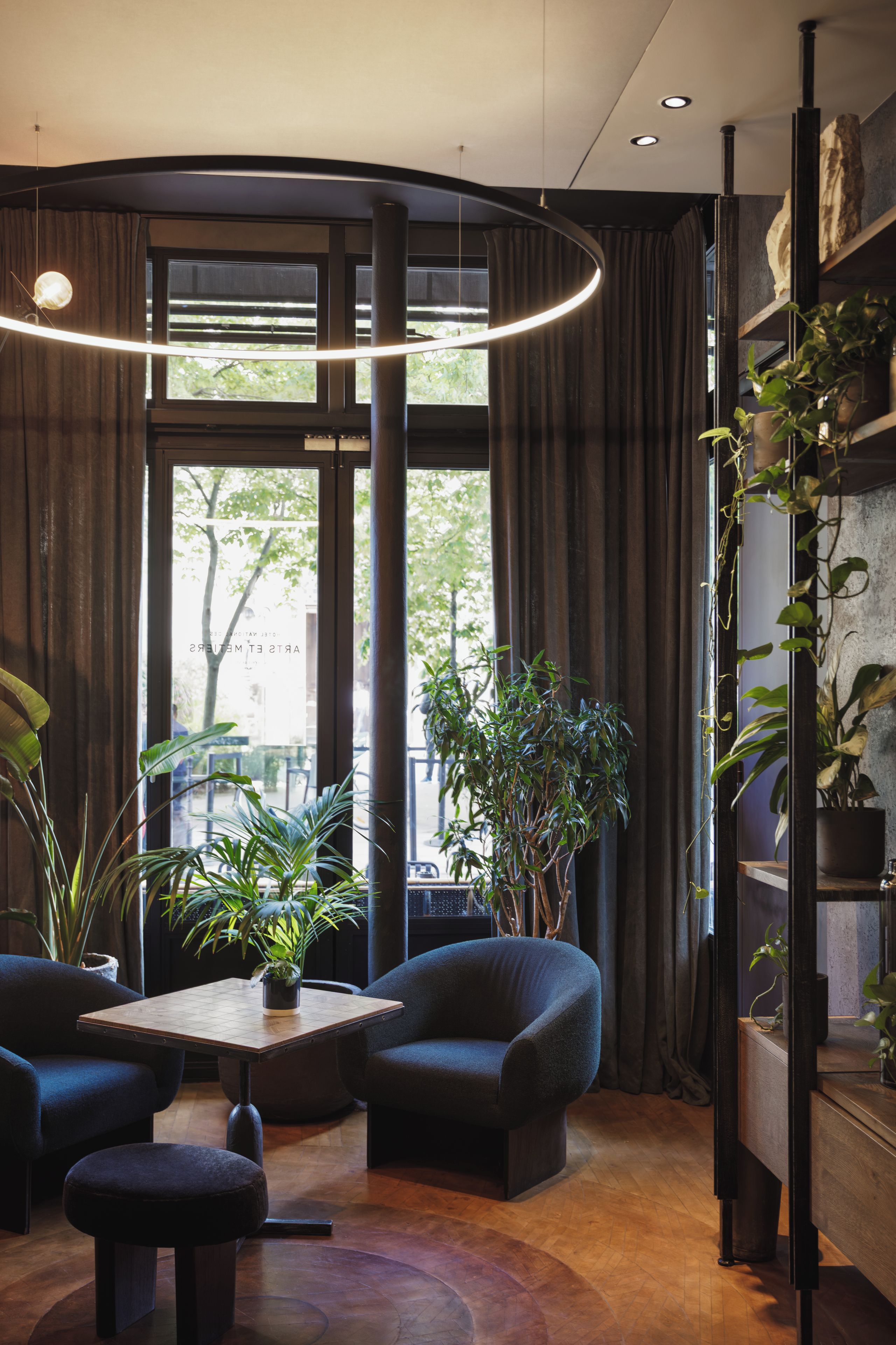 A modern interior with a curved ceiling, a round table, dark sofas, and potted plants.
