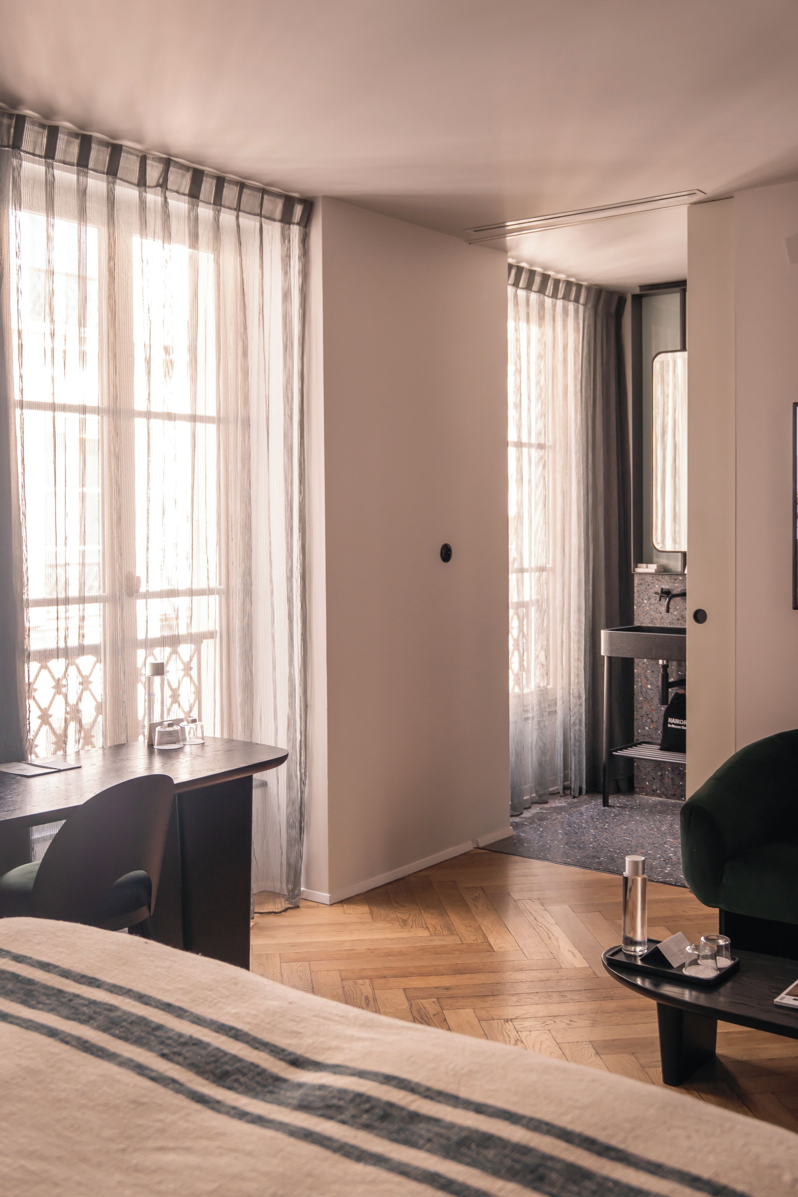 A hotel room with a bed, a desk, and a chair. There is a bathroom visible through an open door.