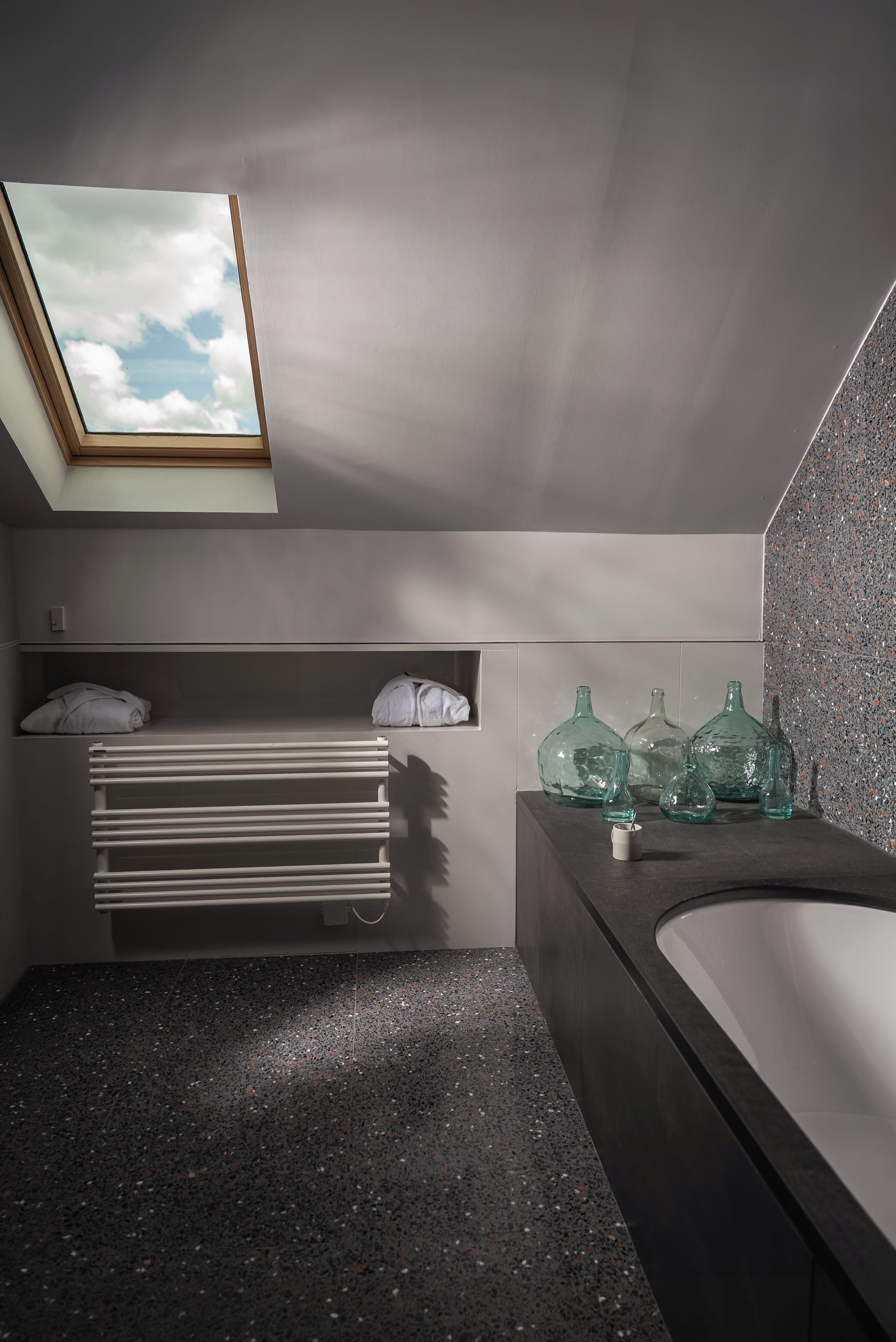 A modern bathroom with a skylight, a built-in towel rack, and a large bathtub.