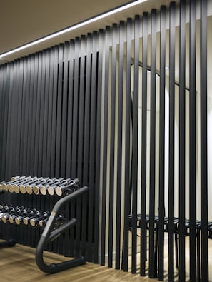 Une salle de sport avec un mur composé de lattes noires verticales et un porte-haltères.
