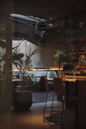 Zona de bar con asientos, una planta grande en maceta y vistas al exterior.