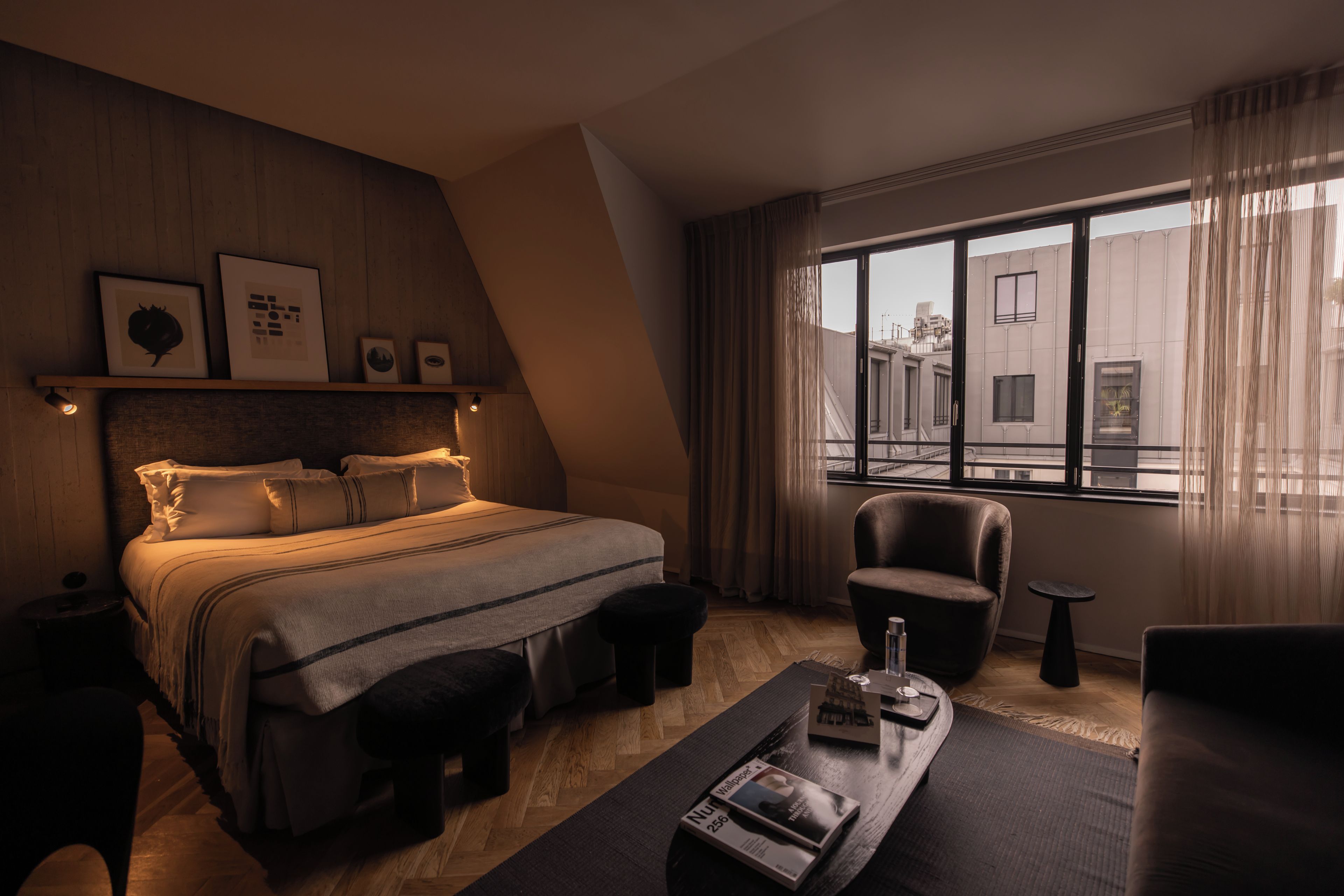 A modern hotel room with a bed, a chair, a small table with a tray, and a large window with curtains.