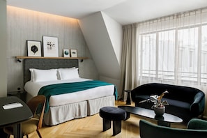 Une chambre d’hôtel moderne, équipée d’un lit, d’un canapé, d’une petite table et d’une chaise. Des tableaux encadrés sont accrochés au mur, au-dessus du lit.