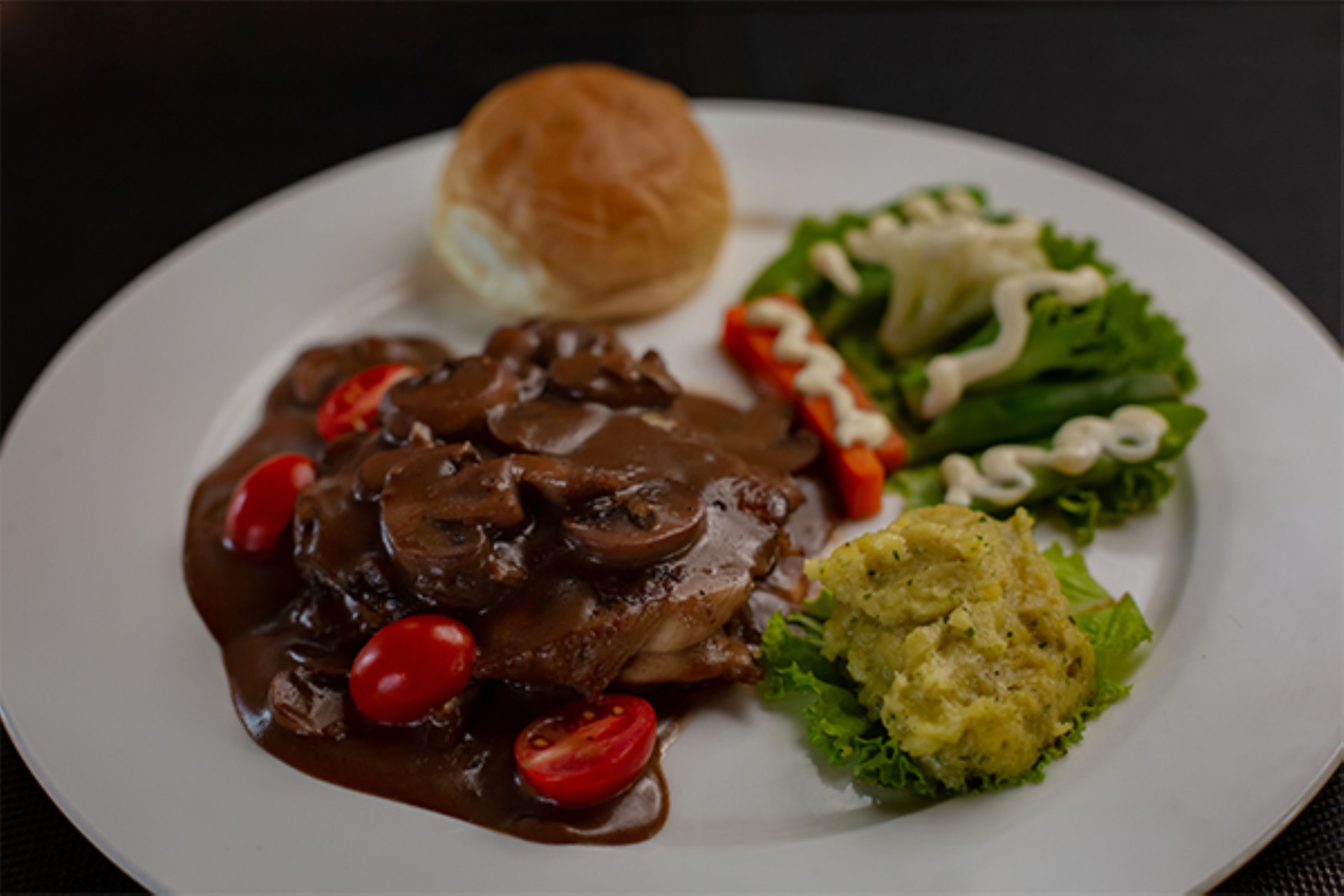 A plate with a meat dish, a side salad, and a roll.