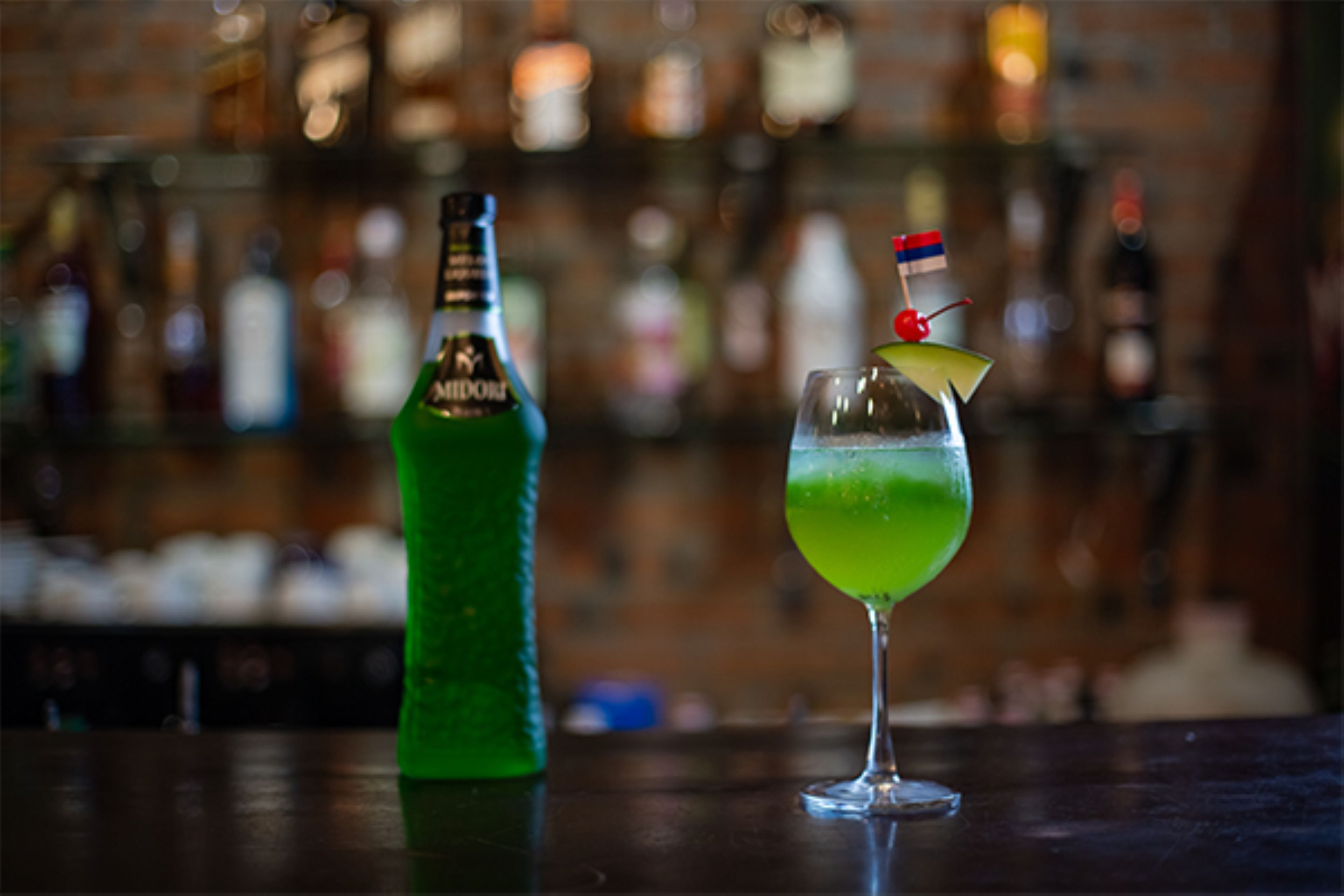 A bar setting with a green bottle and a glass with a cocktail garnish.