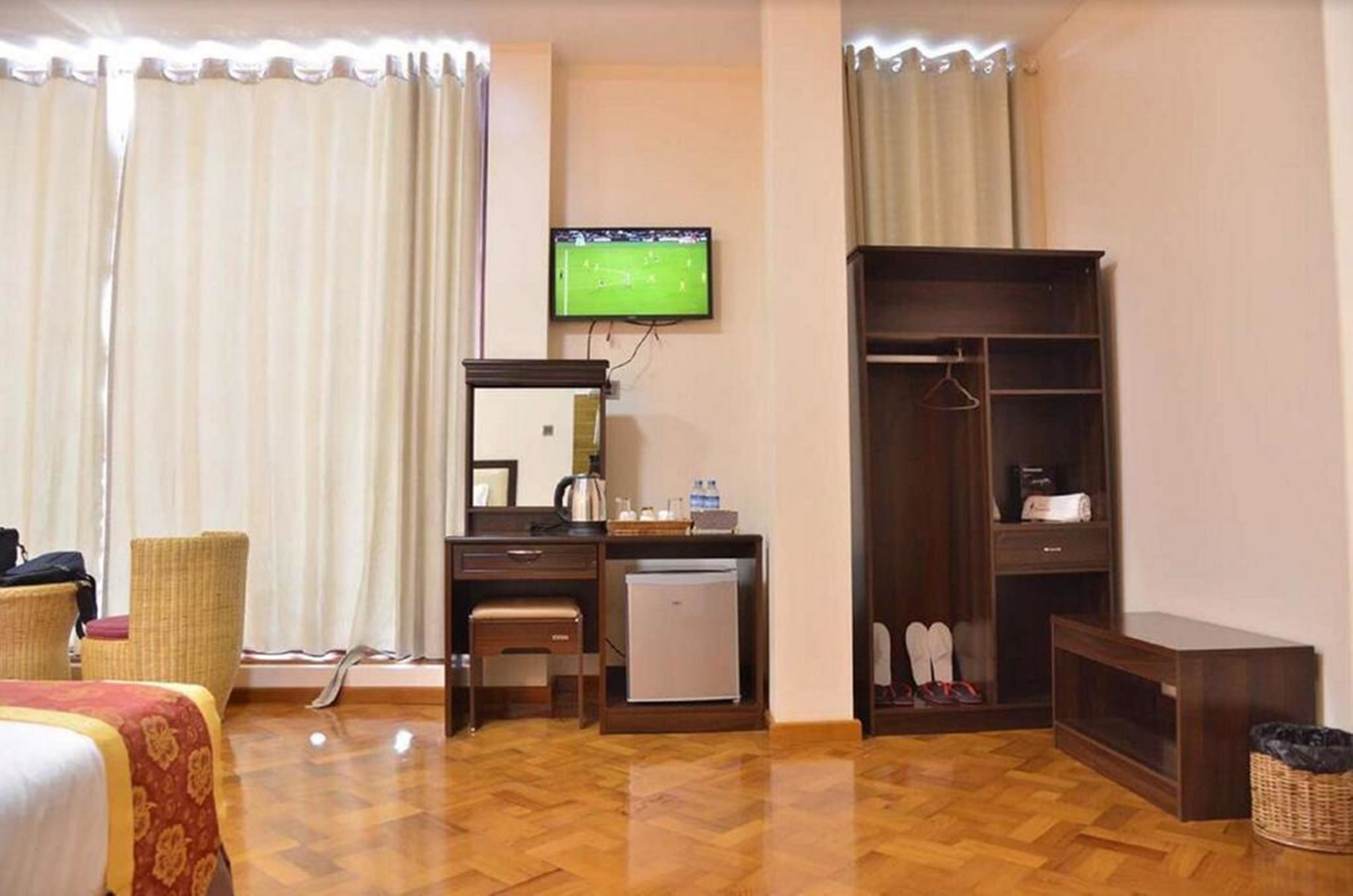 Una habitación de hotel con cama, escritorio con espejo, televisor, armario y un refrigerador pequeño.