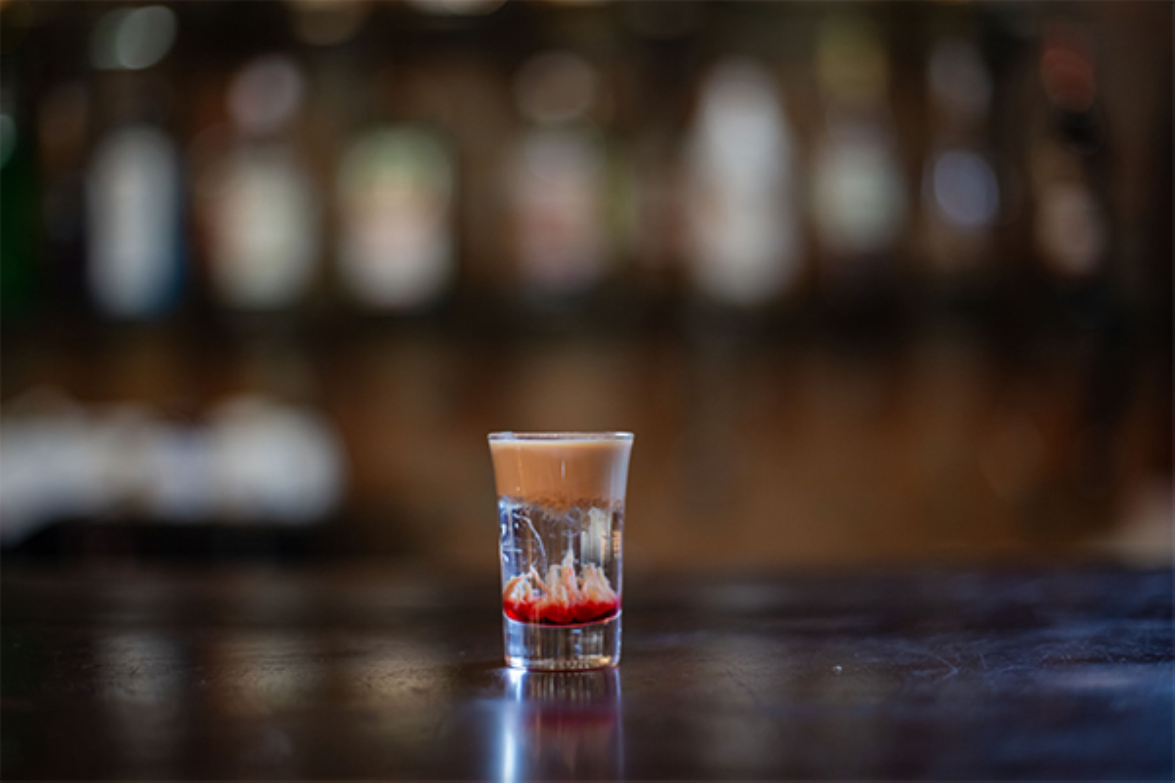 A clear glass with a beverage on a reflective surface.