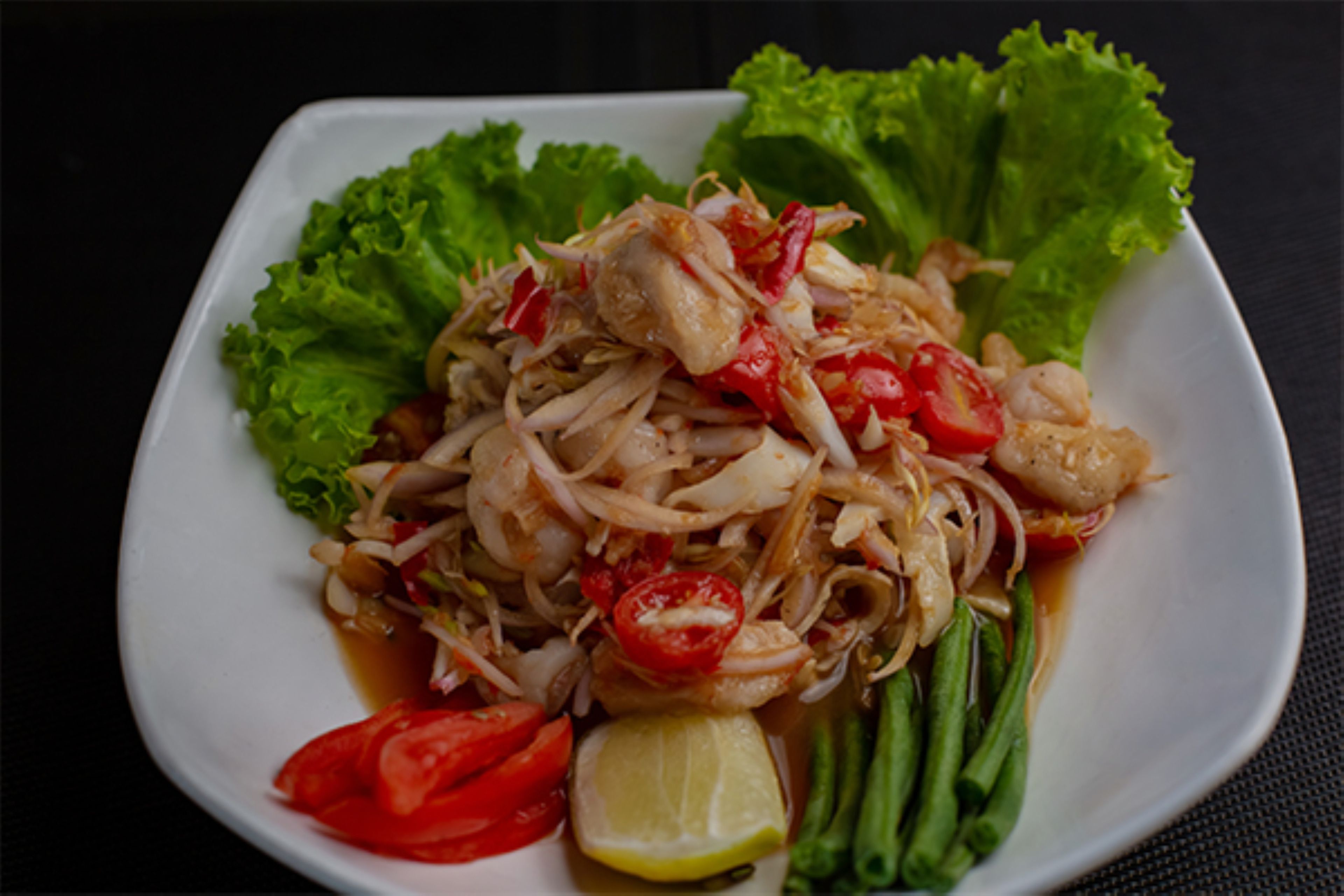 Une assiette de nourriture comprenant des crevettes, des légumes et un quartier de citron vert.