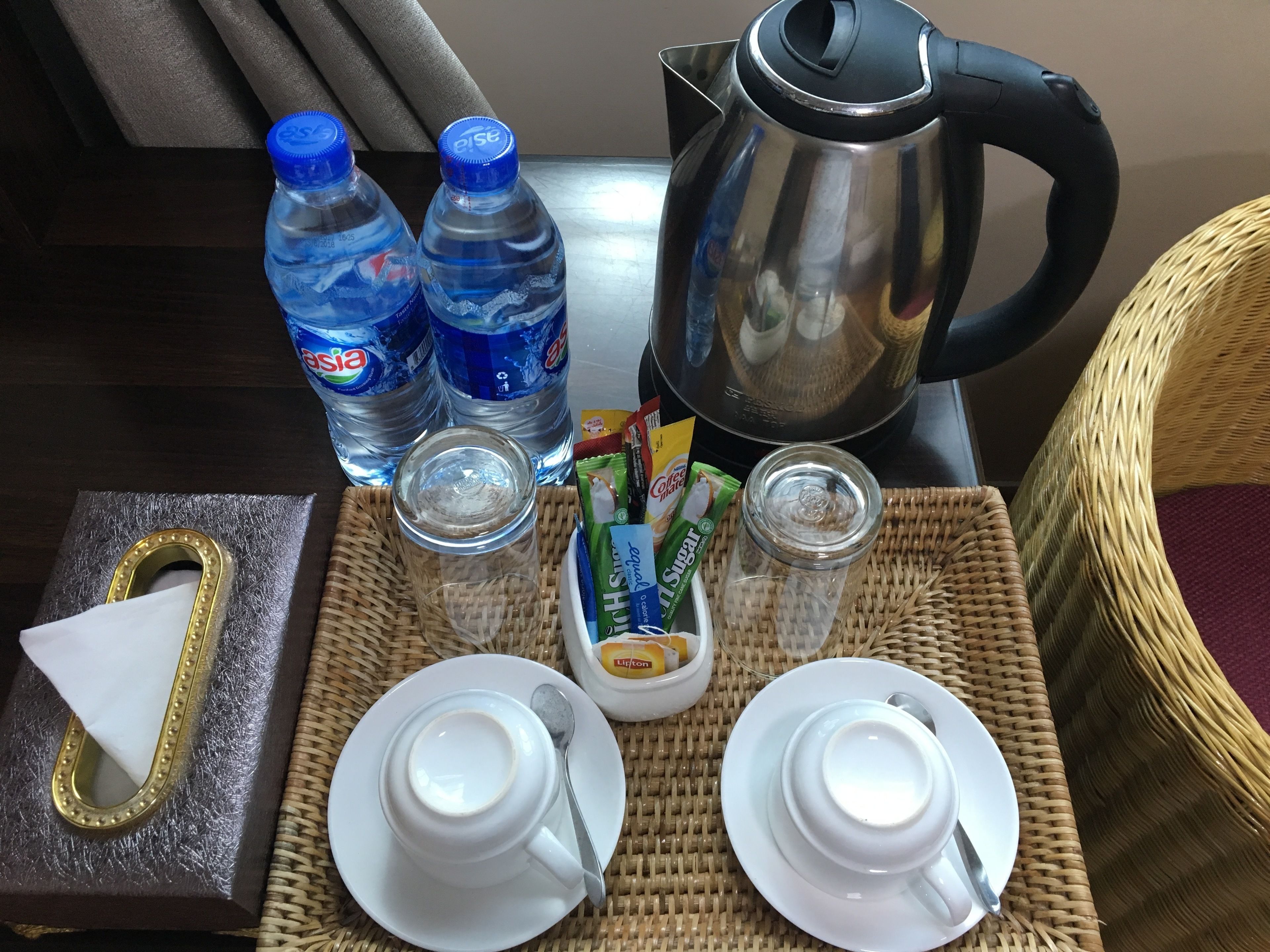 A tray with two cups, two bottles of water, a coffee maker, sugar packets, and a tissue box.