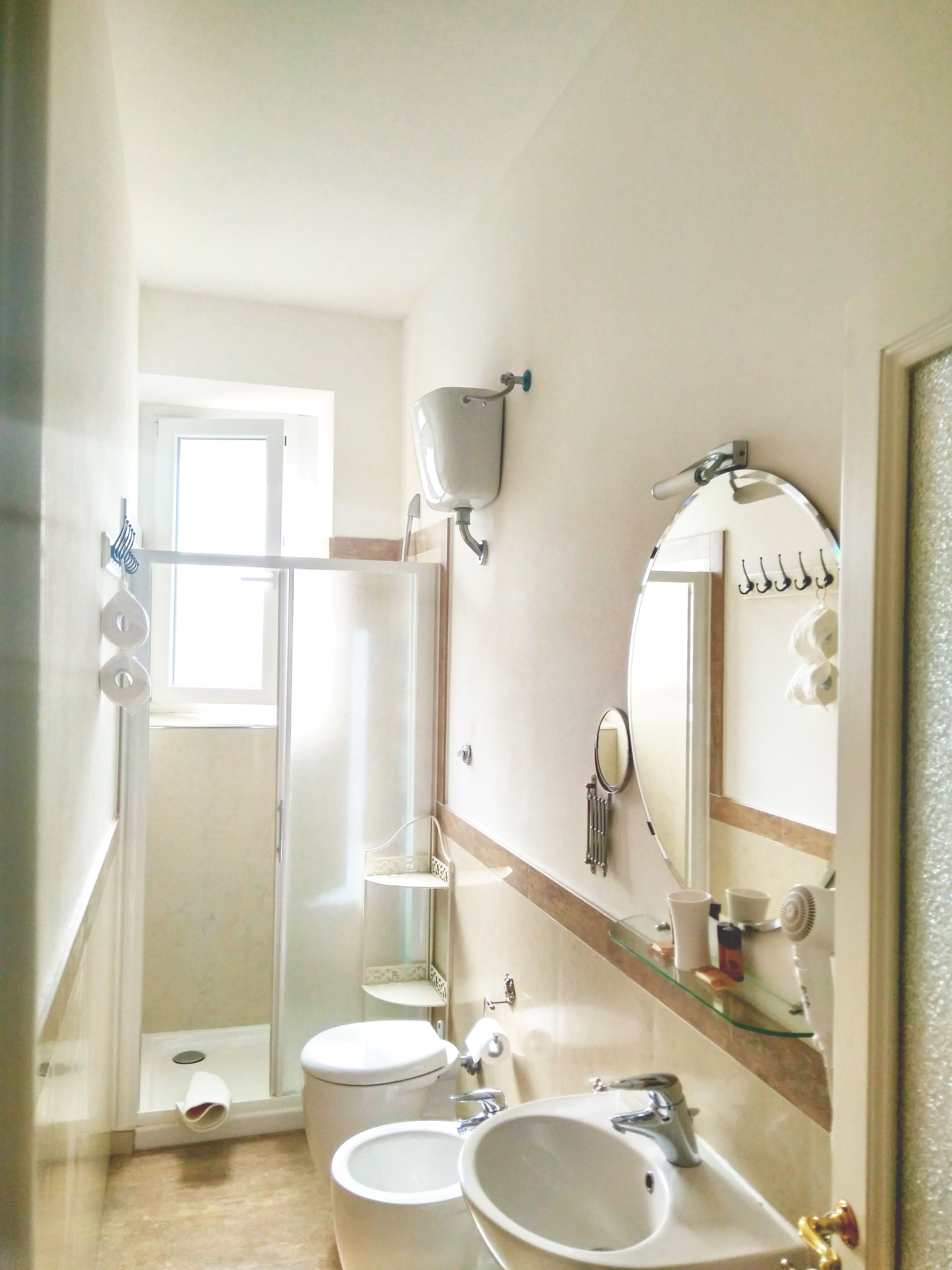 Bany amb vàter, bidet i rentapel. Hi ha una zona de dutxa amb porta de vidre, un mirall i un suport per a tovalloles.
