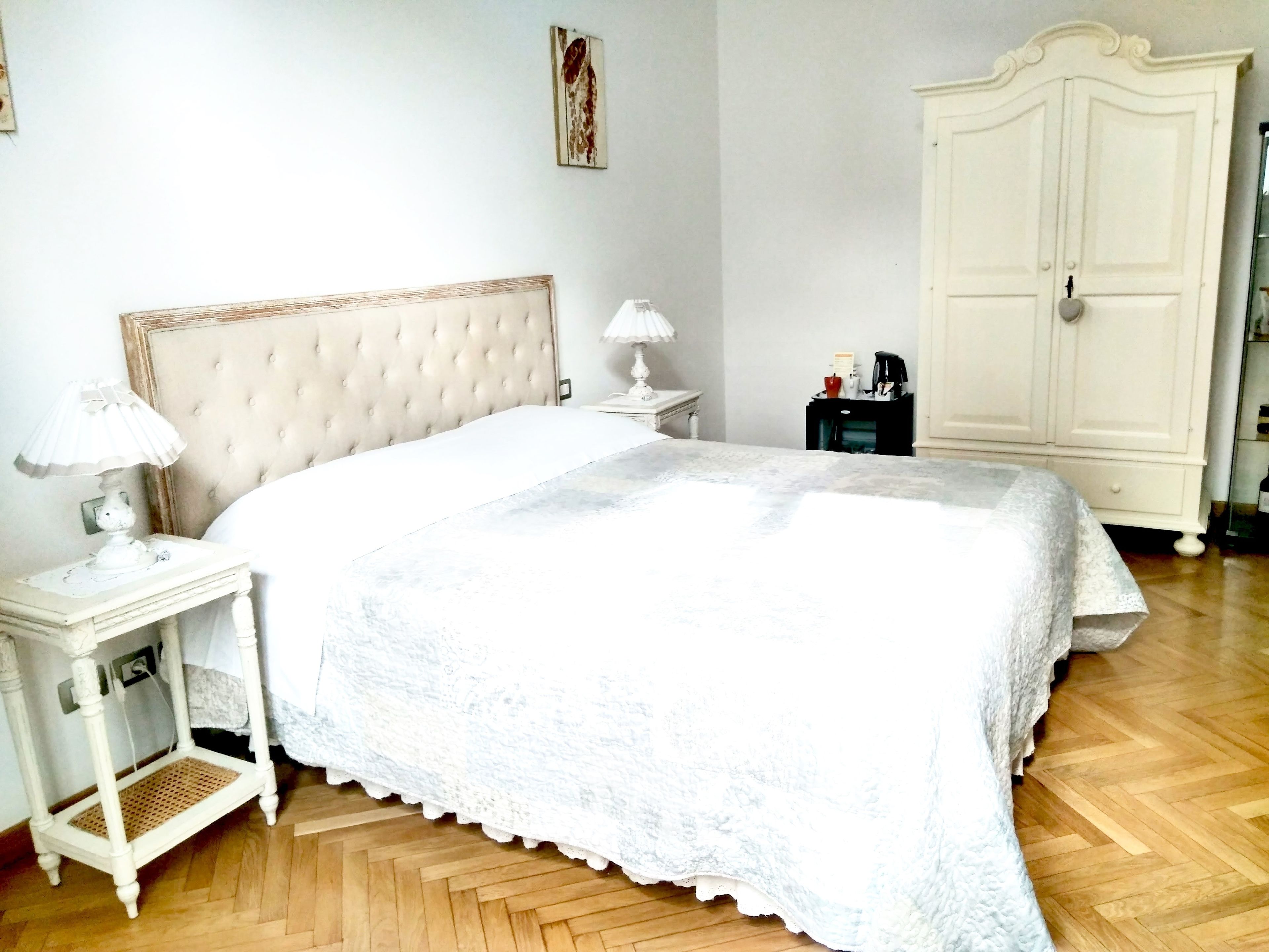 Un dormitorio con una cama grande, una mesita de noche con lámpara, un armario y una pequeña mesa con lámpara.