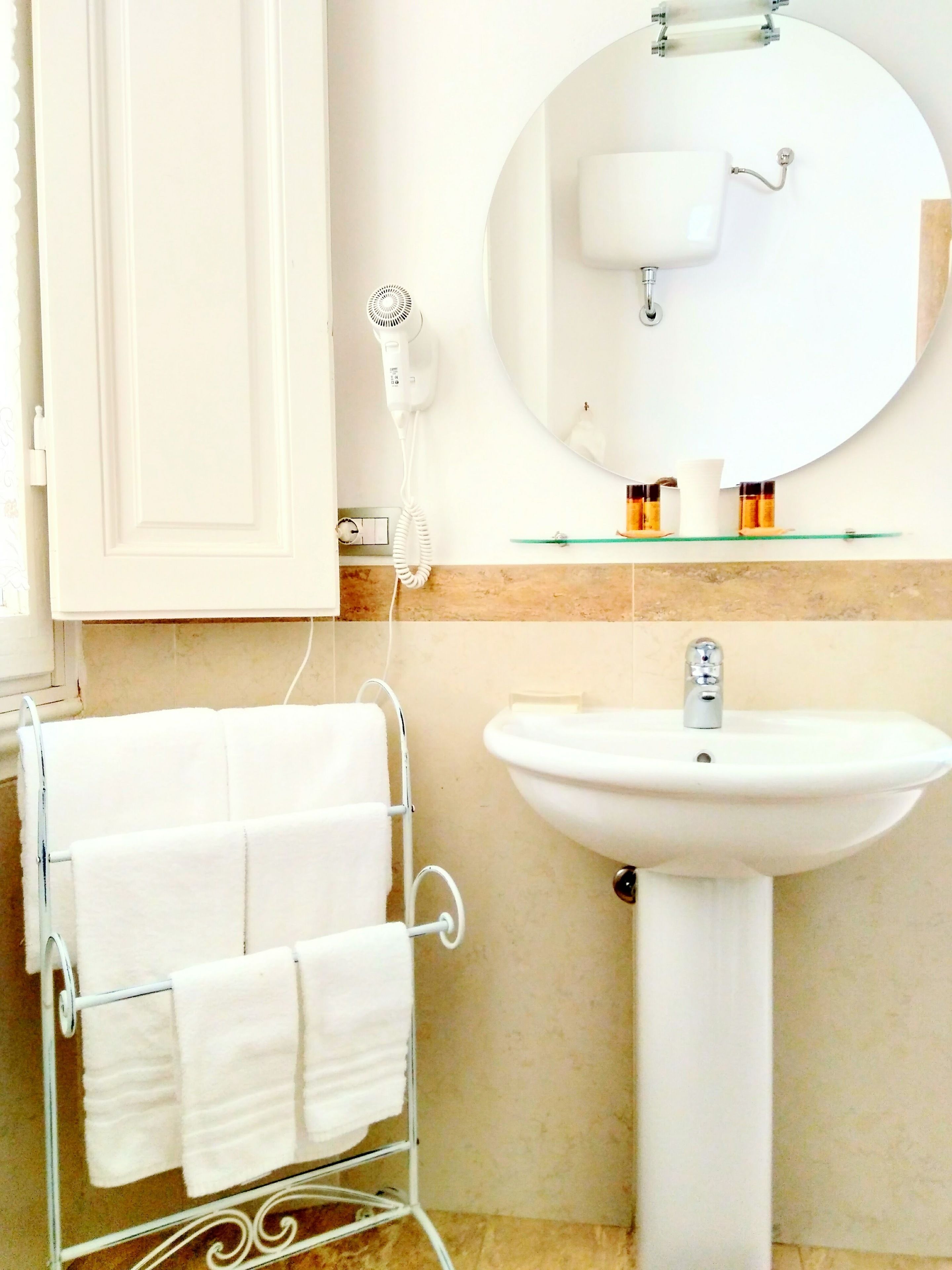 Een badkamer met een wit wastafelmeubel, een ronde spiegel en een handdoekrek met witte handdoeken.