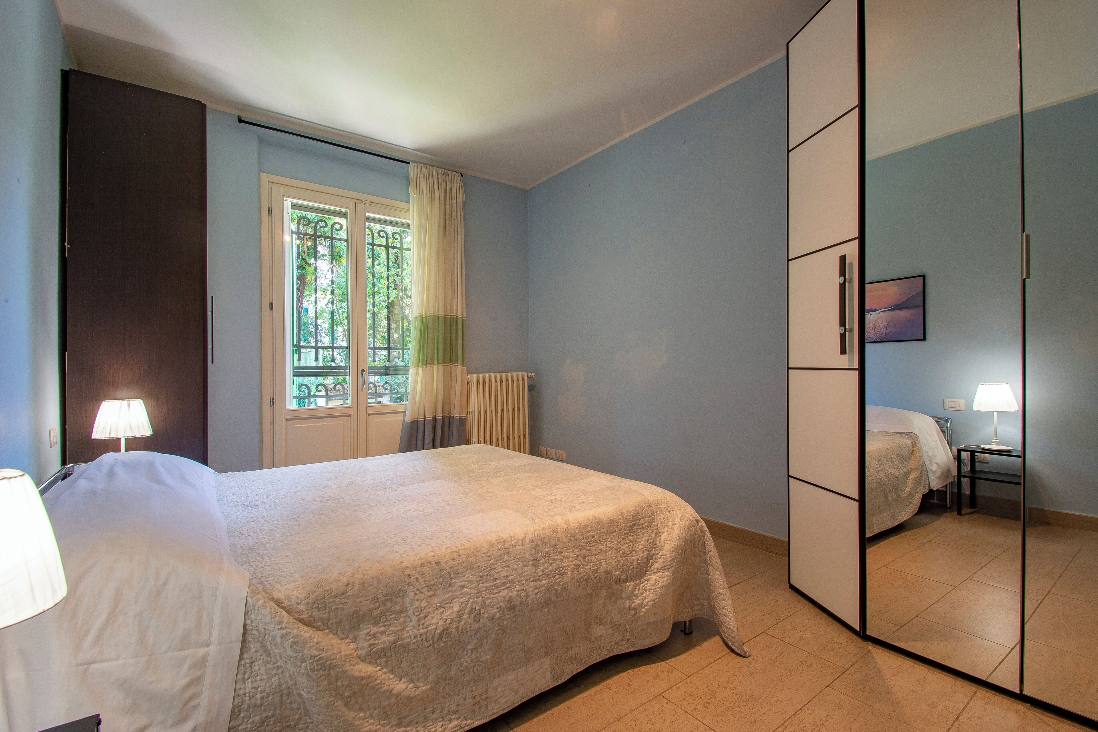 A bedroom with a bed, a wardrobe, a window with curtains, and a radiator.