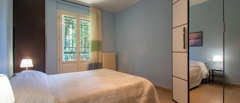 A bedroom with a bed, a wardrobe, a window with curtains, and a radiator.