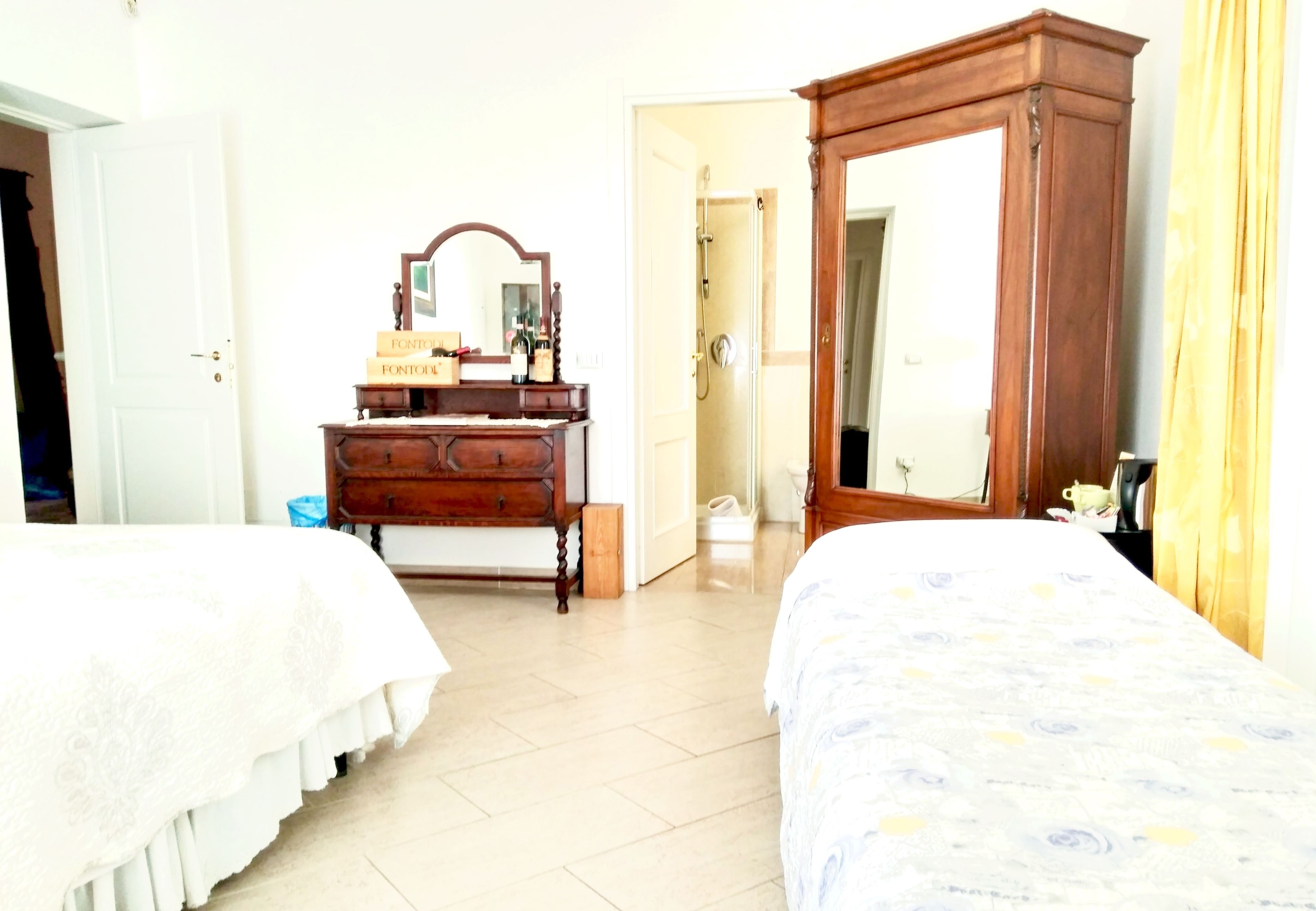 A bedroom with two beds, a wooden dresser, a mirror, and a door leading to a bathroom.