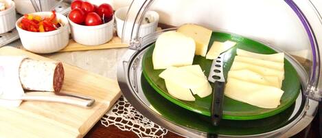A cheese board with various cheeses and a knife, a cutting board with a knife, and a bowl of cherry tomatoes.