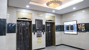 A hotel lobby with two elevators, marble flooring, a chandelier, and a digital display on the wall. - King Hotel (Seongnam)