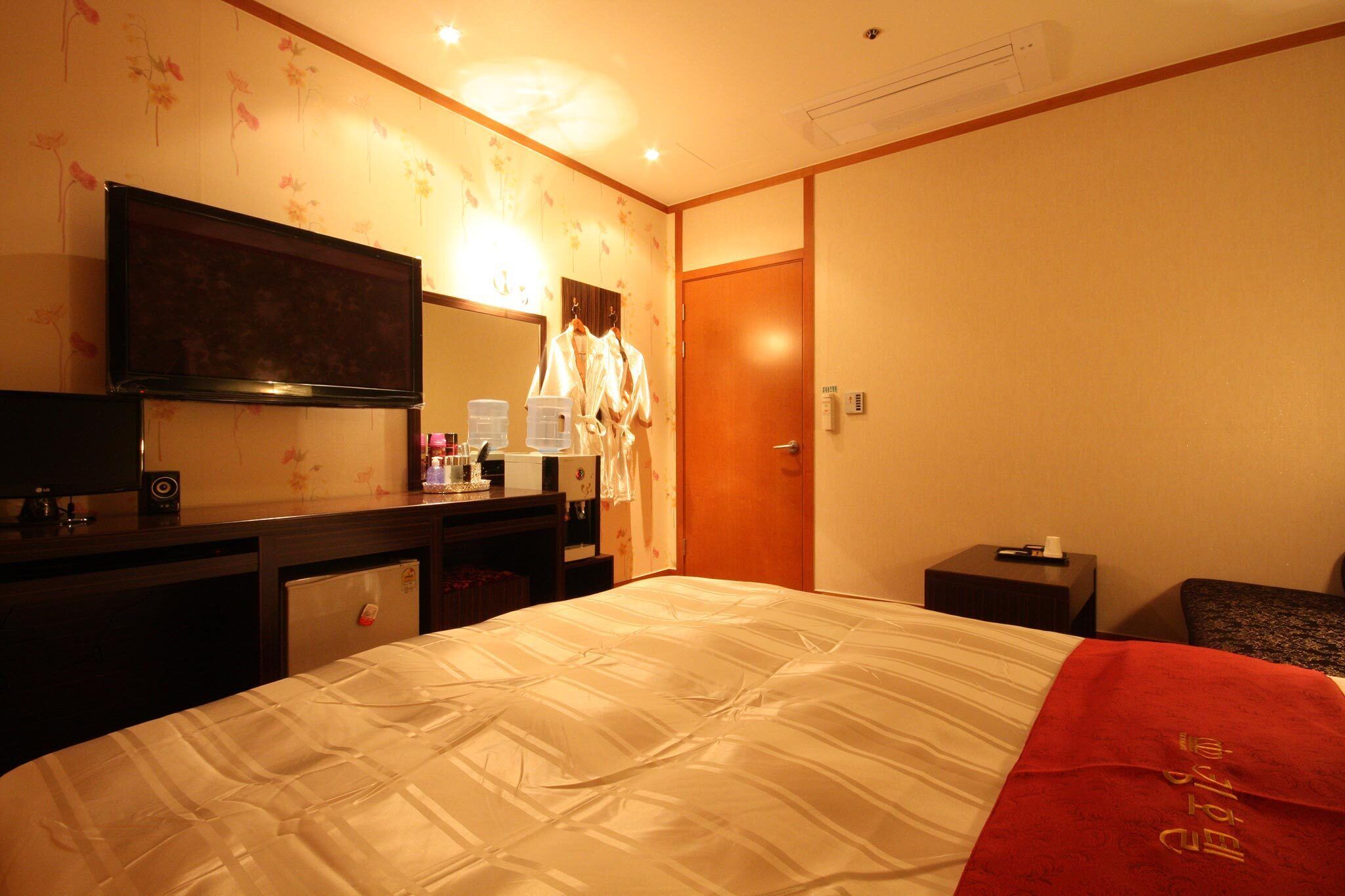 A hotel room with a bed, a TV, a desk with a computer, and a mirror.