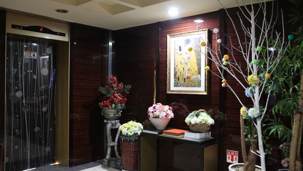 A reception area with a digital elevator display, a framed artwork, and potted plants. - King Hotel (Seongnam)