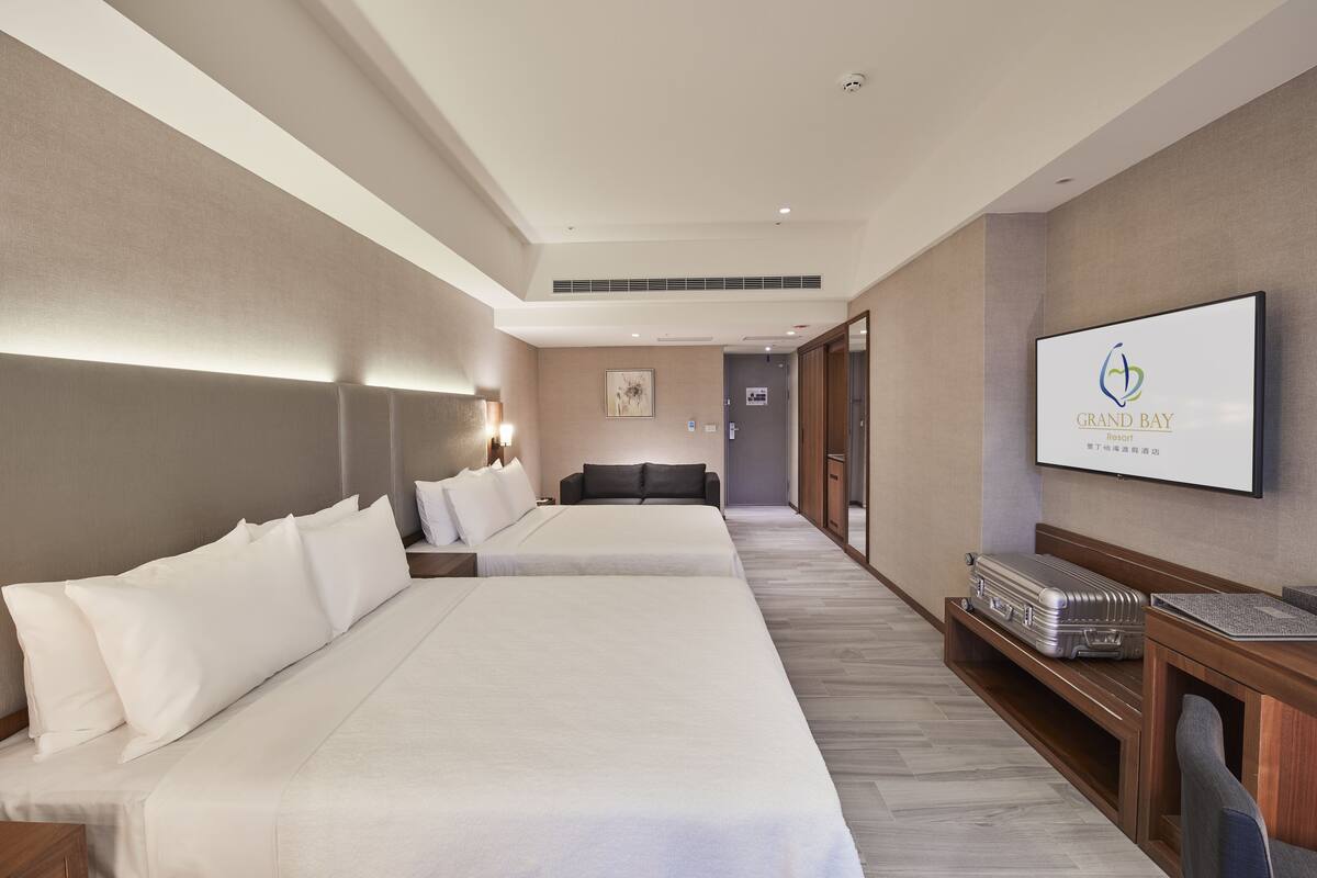 A hotel room with two beds, a TV, a desk, and a suitcase.