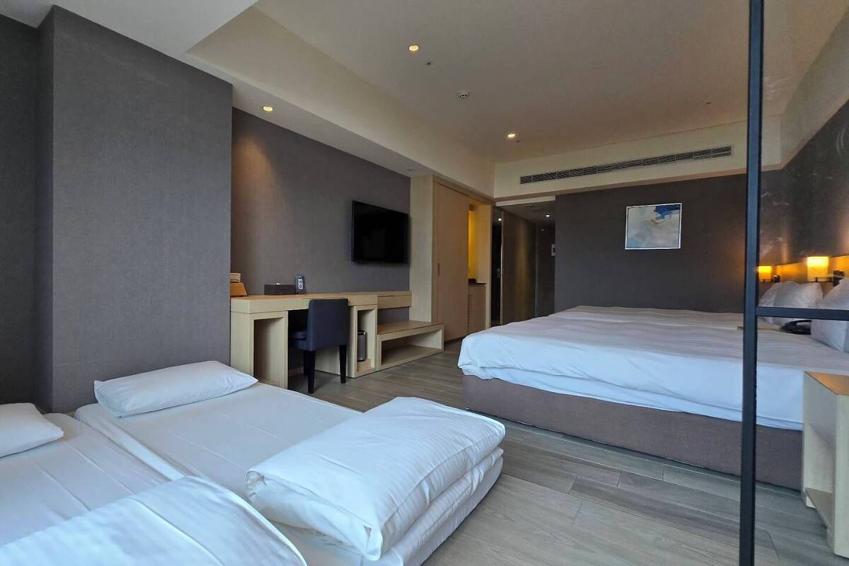 A hotel room with two beds, a desk, a chair, a television, and a mirror.
