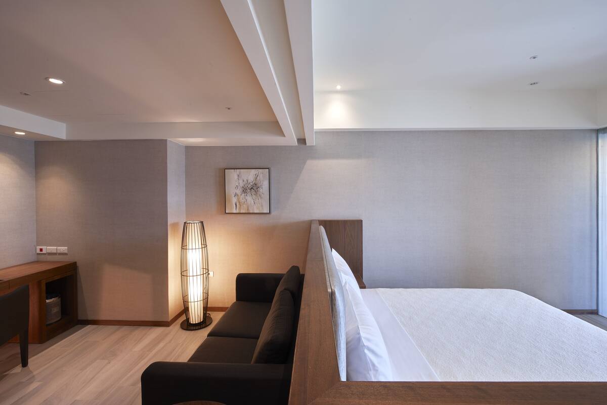 A modern bedroom with a wooden bed, a desk, and a floor lamp.