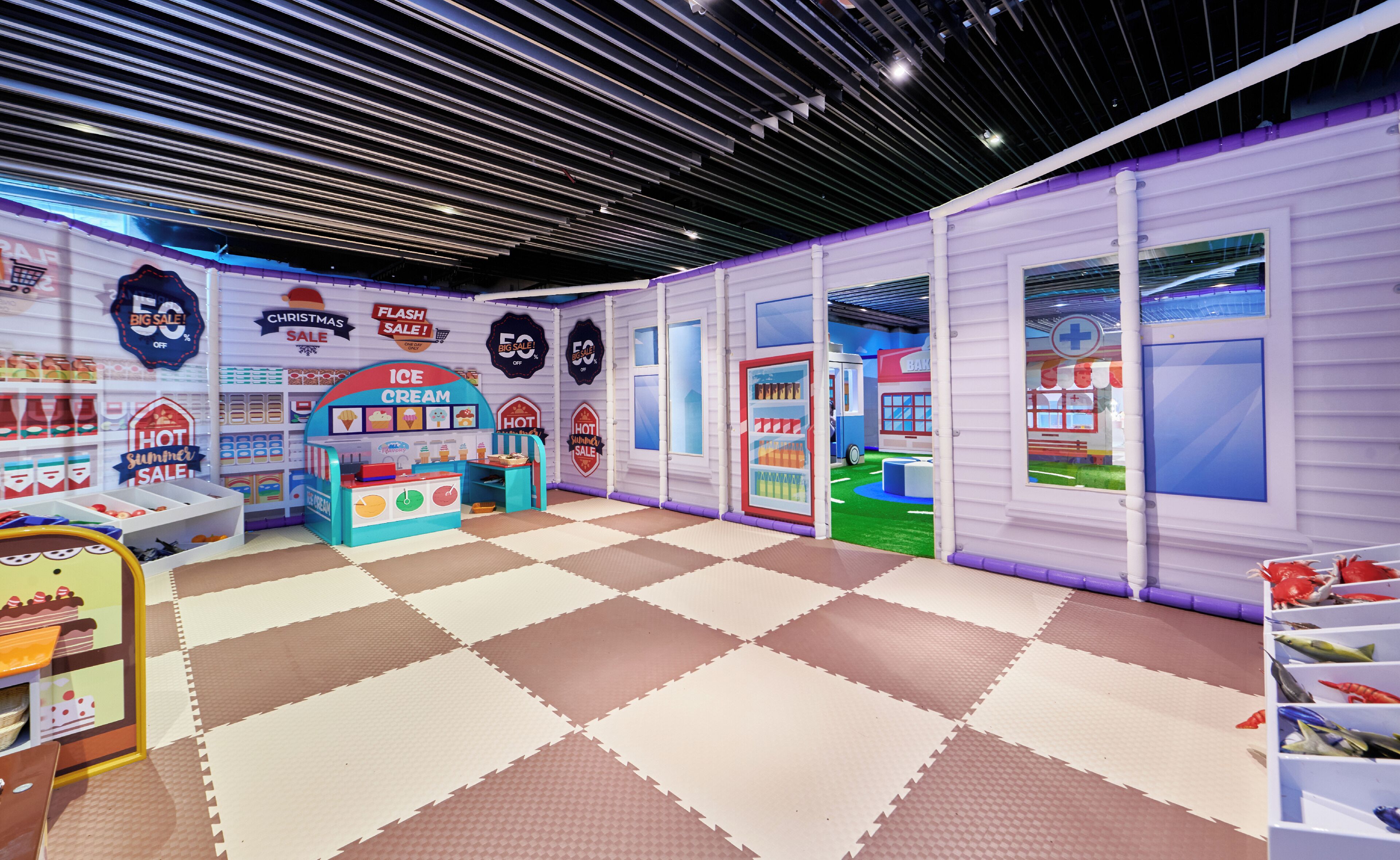 Un'area giochi al coperto con pavimento a scacchi, uno stand di gelateria blu e una panetteria.