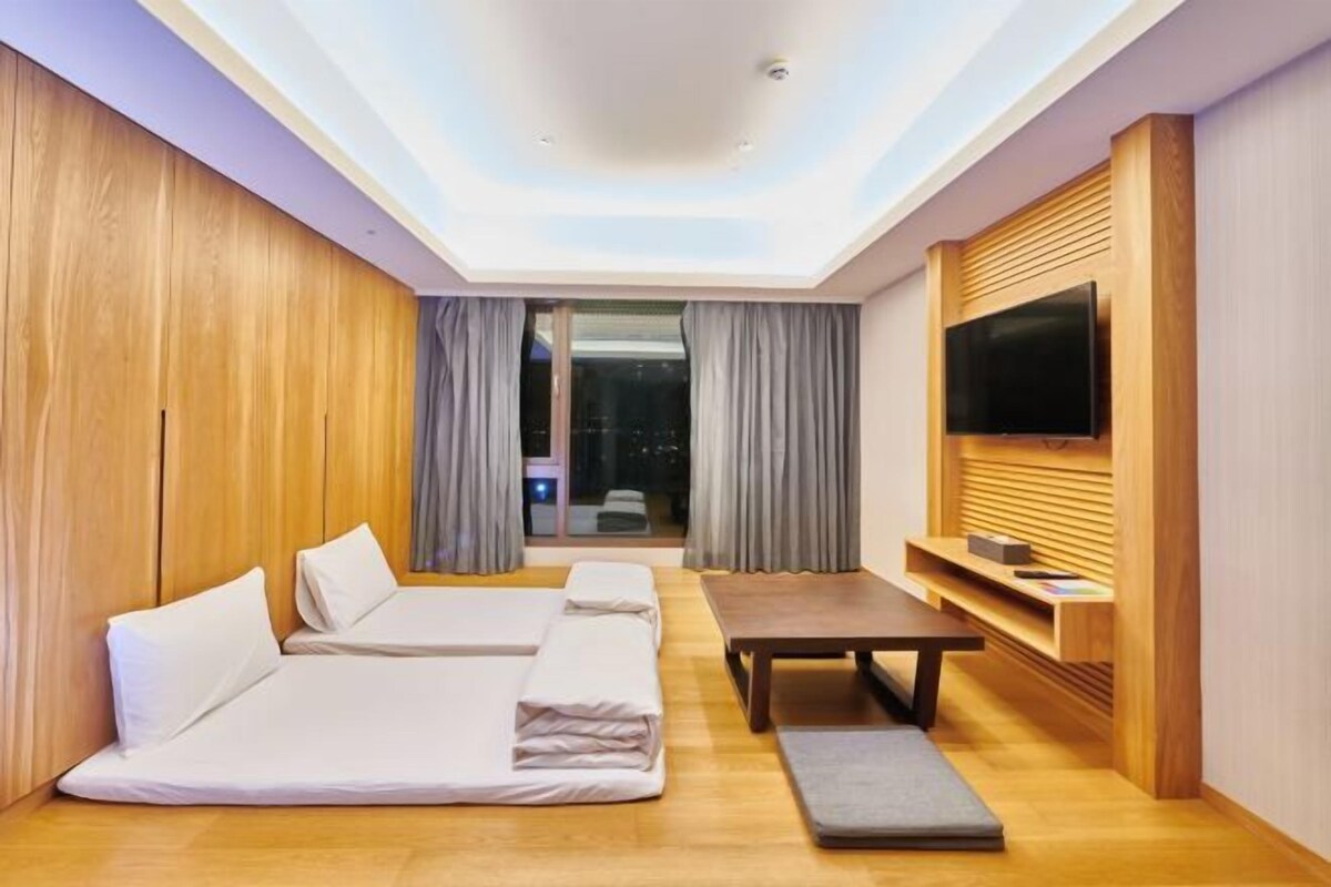 Habitación de hotel moderna con una cama grande, un sofá, una mesita y un televisor montado en la pared.