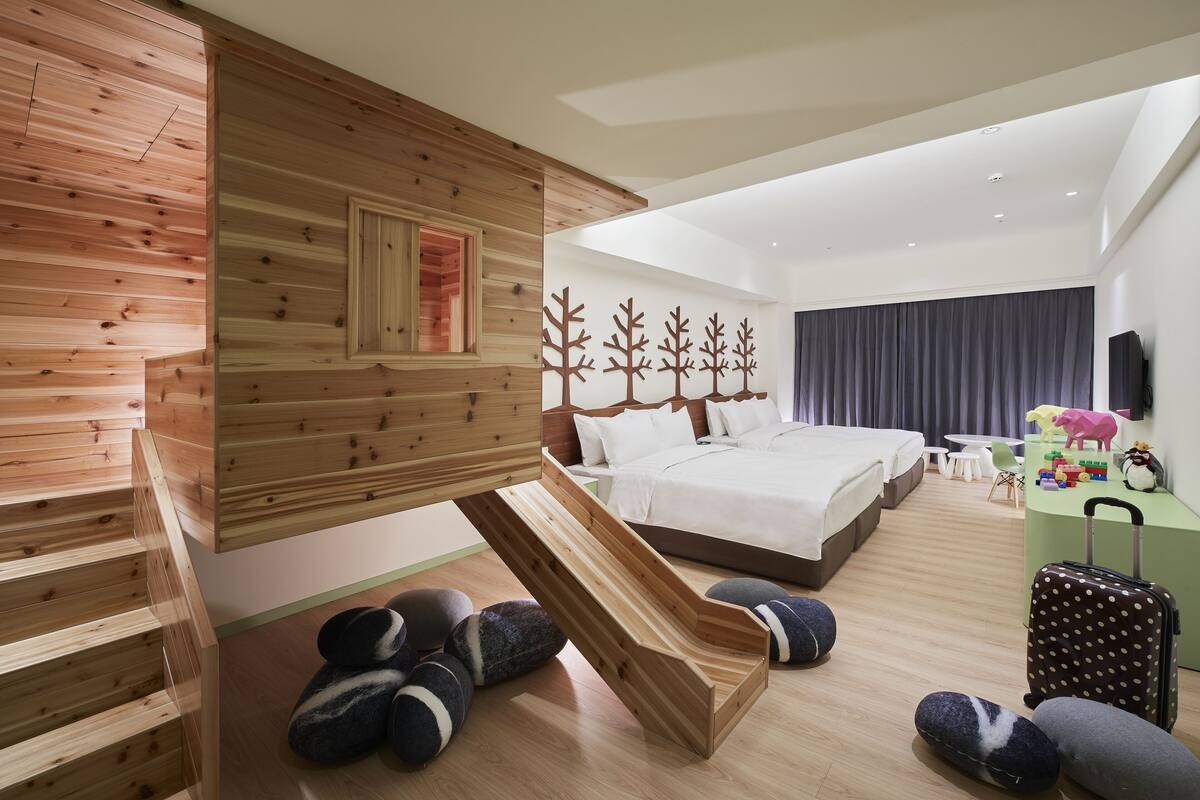 A modern hotel room with a wooden interior, a bed, a desk, and a small seating area with cushions.