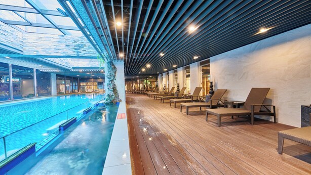 A modern indoor pool area with a wooden deck, lounge chairs, and a glass ceiling. - Grand Bay Resort (Hengchun)