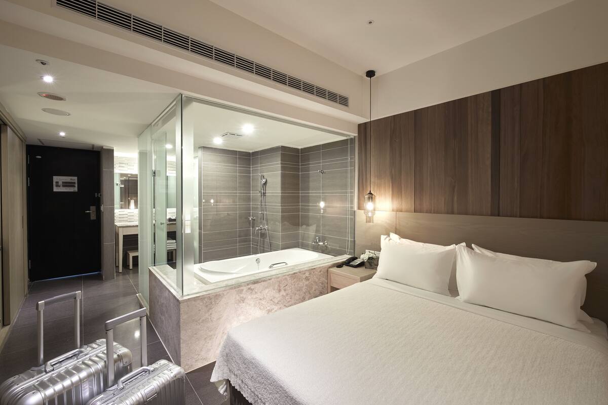 A modern hotel room with a large bed, a glass-enclosed shower, and a wooden headboard.