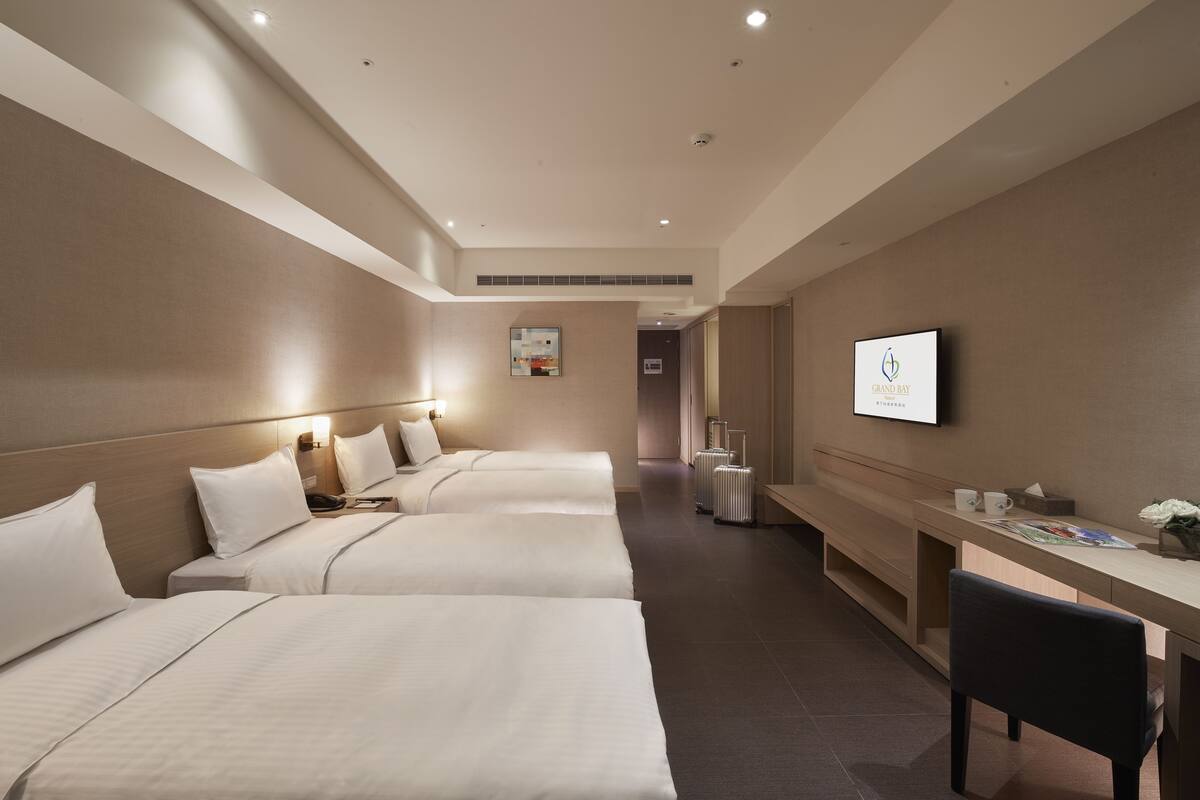 A hotel room with three beds, a desk, and a television.