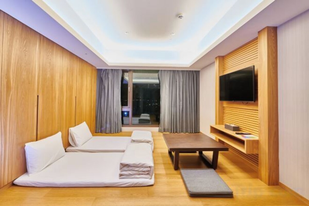 Una habitación de hotel moderna con una cama grande, un pequeño sofá, una mesa de comedor y un televisor montado en la pared.