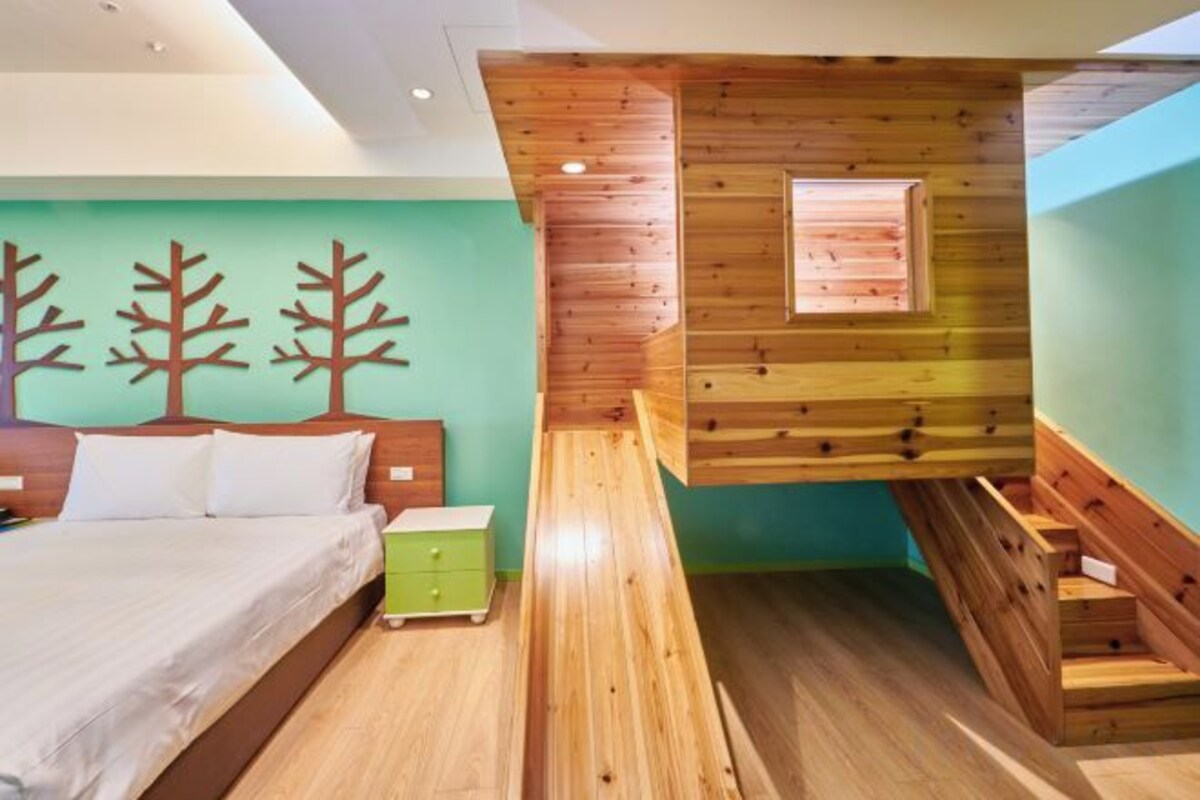 Un dormitorio con una cama, una mesita de noche, un cajón verde, un banco de madera y una ventana.