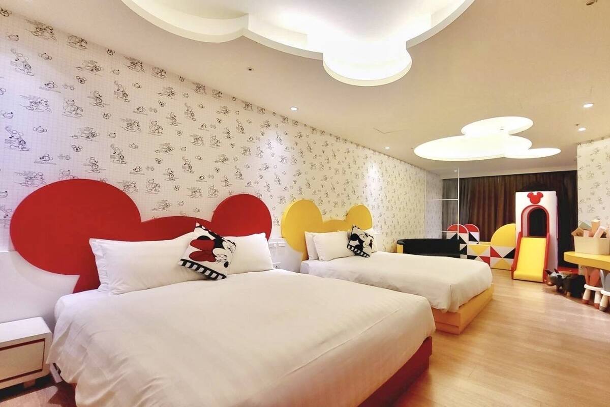 A hotel room with two beds, a large mirror, a small desk, and a play area with toys.